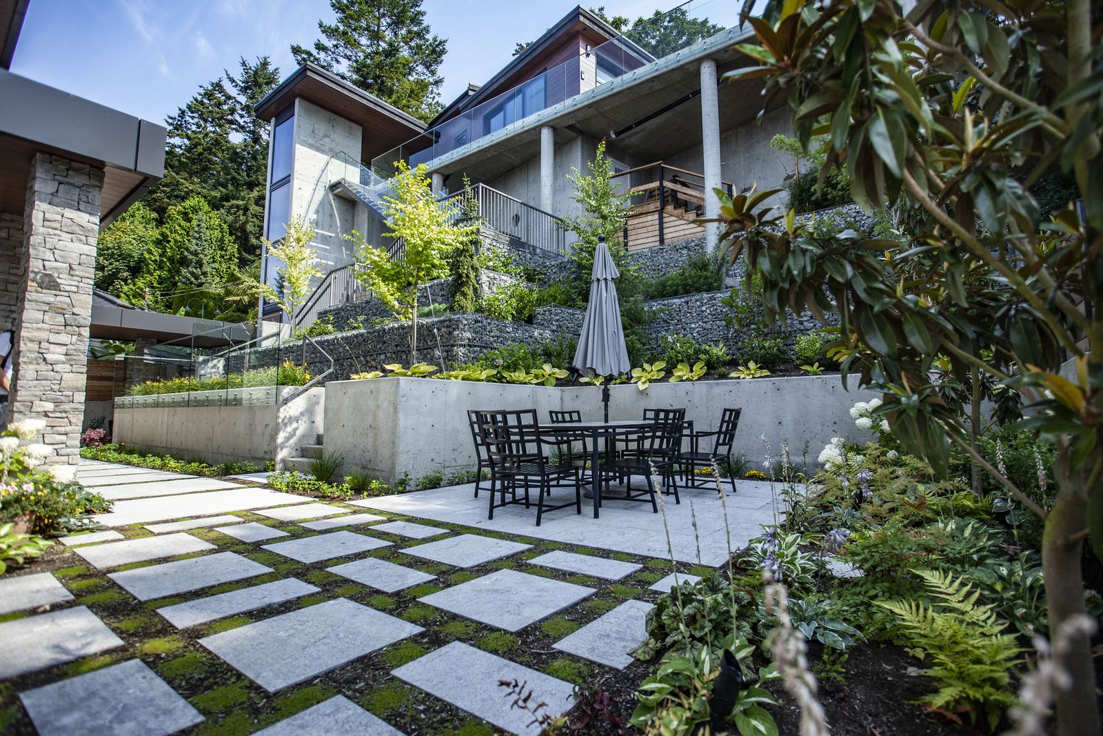 Tiered backyard with a slab and moss patio, board-form concrete walls and a dining set